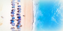 Top down view of a beach with tourists suntbeds and umbrellas with sand beach and clear blue water in Greece