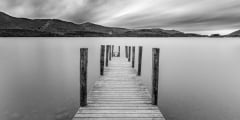 Long wooden jetty at Derwentwater Lake with moody dramatic cloud