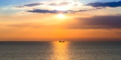 Sunset over seacoast with small fishing boat, natural landscape