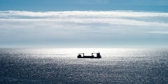 Small freight ship shows as a silhouette against the bright reflection from the sun. West Cape, Stad, Norway